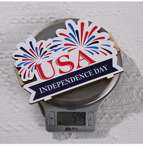 Weight measurement of Independence Day USA wooden sign showing 57.4g on a digital scale