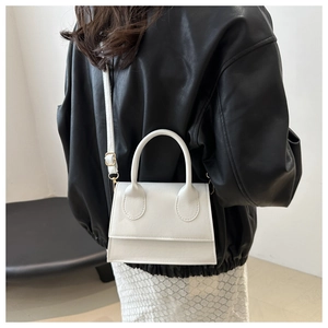 Close-up of a white minimalist leather crossbody bag with top handle and golden buckles