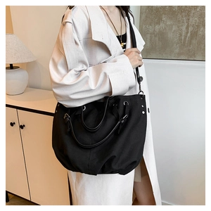 Detail of black canvas tote bag showing metal rivets and premium leather handles