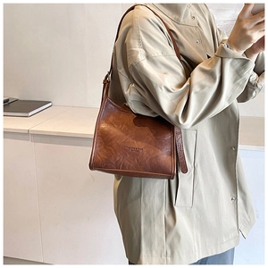 Close-up of vintage brown leather tote bag with embossed logo on minimal light trench coat