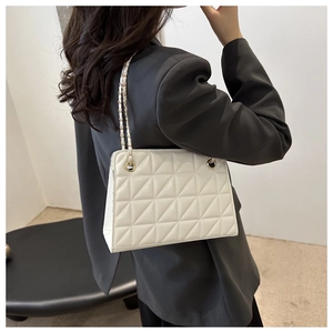 Detail of white quilted crossbody bag with gold chain strap worn over a grey blazer