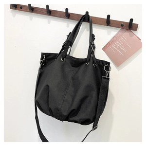 Detail of black canvas tote bag with metal buckles and adjustable strap hanging on a wooden hook