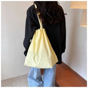 Detail of a vibrant yellow drawstring tote bag with natural fabric texture on a model