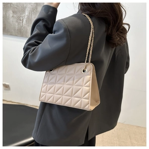 Detailed side view of beige quilted crossbody bag with gold chain strap on model
