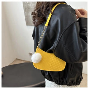 Detail view of bright yellow quilted half-moon shoulder bag with plush ball charm