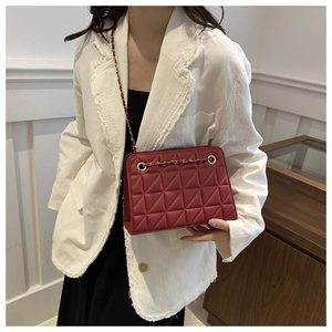 Detail of burgundy quilted chain bag with gold hardware worn by a model in casual setting