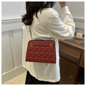 Detail of dark red quilted crossbody bag with gold chain strap on model's shoulder