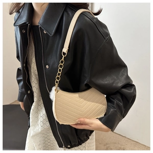 Detail of beige quilted baguette bag with V-shaped stitching and golden chain strap