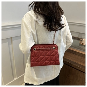 Detail view of a red quilted chain crossbody bag worn on shoulder for size reference