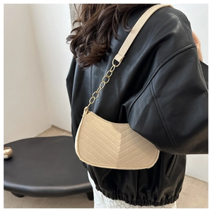Detail of beige quilted crescent bag with gold chain strap on a black leather jacket