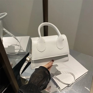 Minimalist white leather crossbody bag with round handle shown against a mirror backdrop