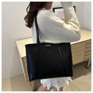 Detail of black large capacity faux leather tote bag with fashion label on a model