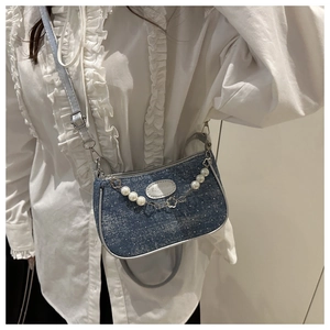 Blue denim crossbody bag with pearl chain and floral charms shown on white shirt