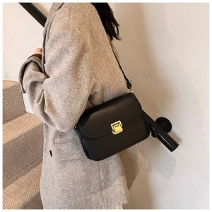 Close-up of a black leather crossbody bag with a vintage gold square clasp on a grey coat