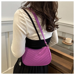 Detail of purple quilted baguette bag with V-shaped stitching worn on the shoulder