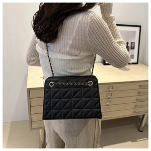 Detail of a black quilted crossbody bag with a gold chain strap worn by a model