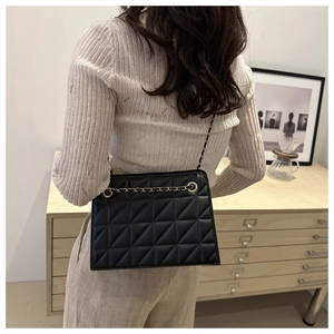 Quilted black leather shoulder bag detail with gold chain strap shown on person