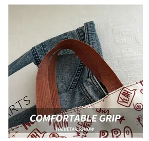 Detail of sturdy brown canvas strap and red graffiti print on a white tote bag