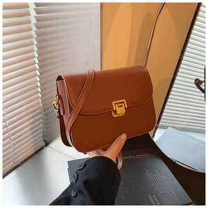 Close-up of brown leather crossbody bag featuring a modern gold square buckle closure