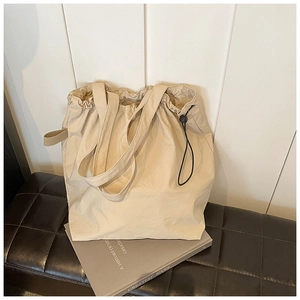 Detailed view of beige drawstring canvas tote bag with black adjustable cords on books