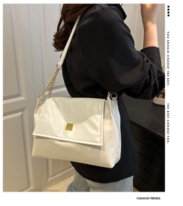 Detail of white leather shoulder bag with golden metal chain strap and square lock clasp