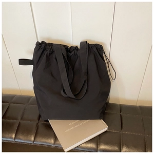 Close-up of black nylon drawstring tote bag on a brown leather bench with a minimalist look