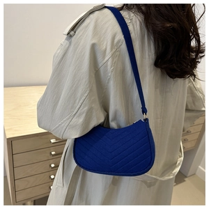 Blue chevron quilted baguette shoulder bag worn over a beige trench coat for women