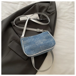 Detail of blue denim crossbody bag with silver piping on a dark grey suit jacket