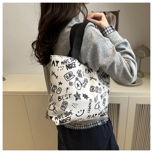Detail of canvas tote bag featuring graffiti prints and black shoulder strap on model