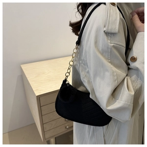 Detail of minimalist black hobo bag with gold chain strap and fluffy pompom charm