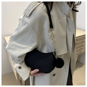 Detail of black V-quilted hobo bag with gold chain strap and plush ball pendant charm