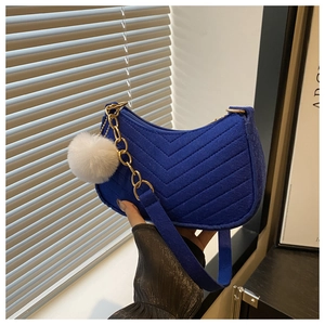 Close-up of blue quilted saddle bag with silver chain and white fluffy ball pendant