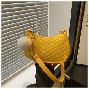 Macro shot of yellow crescent bag featuring V-quilting detail and a white pom-pom