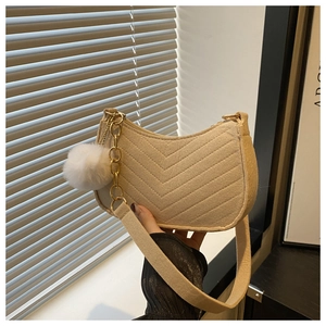 Detail of beige chevron-quilted crescent bag with golden chain and plush pompom charm