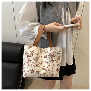 Detail of canvas tote bag featuring brown graffiti print and woven carrying handles