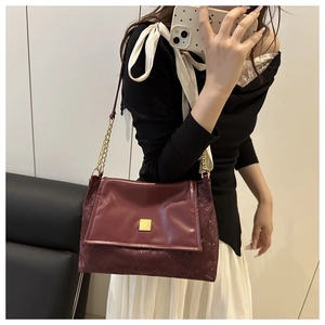 Detail of burgundy leather shoulder bag with golden buckle and subtle animal texture