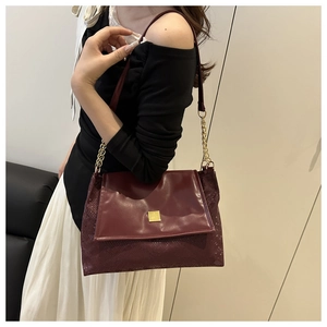 Detail of burgundy leather tote with snake pattern and gold buckle on a model
