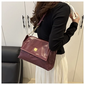 Detail of burgundy shoulder bag with snake pattern texture and gold chain strap on model
