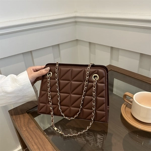 Deep brown quilted crossbody bag with gold chain strap in a cozy cafe setting