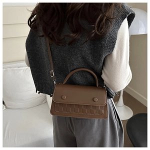 Detail showing brown textured leather bag with handle and adjustable shoulder strap