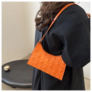 Detail view of bright orange baguette bag with embossed texture and gold zipper hardware