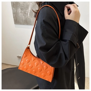 Detailed view of orange quilted shoulder bag with scalloped pattern on a model