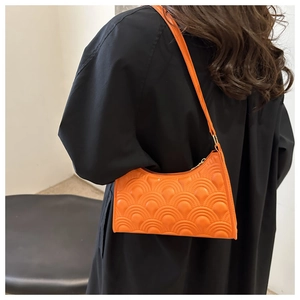 Detail of orange baguette shoulder bag with quilted fish scale texture on dark outfit