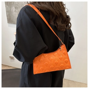 Rear view of a model wearing a bright orange quilted hobo shoulder bag with wave pattern