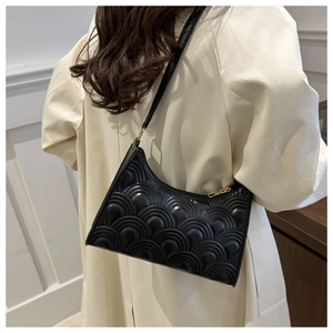 Detail of black baguette bag with fish scale quilting worn over a beige trench coat