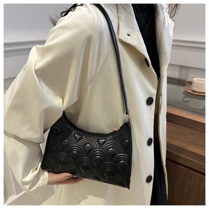 Detail of black quilted shoulder bag with wavy stitching worn with a beige trench coat