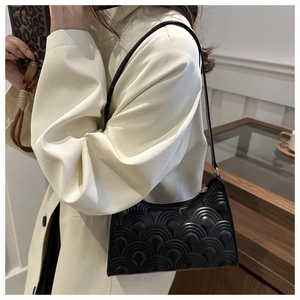 Detailed side view of a black quilted leather shoulder bag worn over a neutral outfit