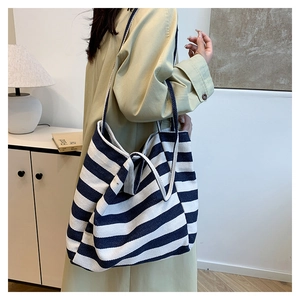 Detail of a large blue and white striped canvas tote bag worn by a model in a minimal room