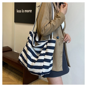 Detail of striped canvas tote bag with thick woven rope handles shown on shoulder