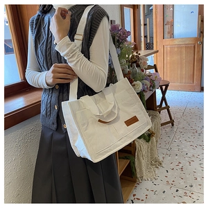 Detail of white corduroy tote bag showing broad strap and brown leather label